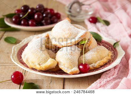 Pies With Cherries, Sprinkled With Powdered Sugar And Berries Of Fresh Cherries On A Wooden Surface.