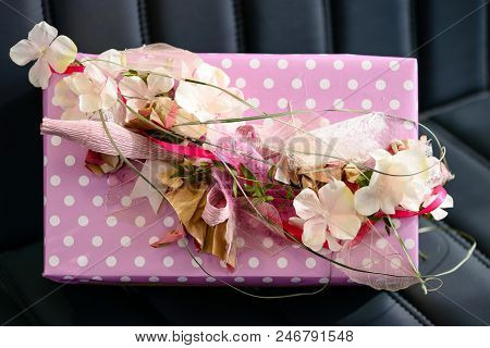 Handmade Gift Box Wrapped With Pink Paper And Decorated With Ribbon And Flowers On Dark Leather Sofa