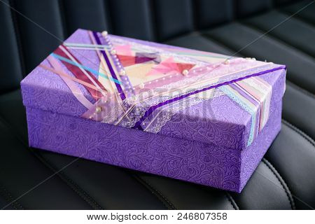 Handmade Gift Box Wrapped With Purple Paper And Decorated With White Beads On Dark Leather Sofa