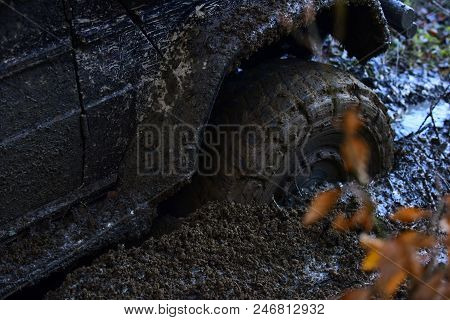 Offroad Tire Covered With Mud Overcomes Obstacles On Nature Background. Wheel In Deep Puddle Of Mud.