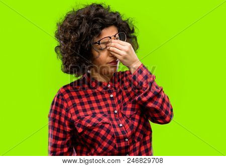 Beautiful arab woman with sleepy expression, being overworked and tired, rubbes nose because of weariness