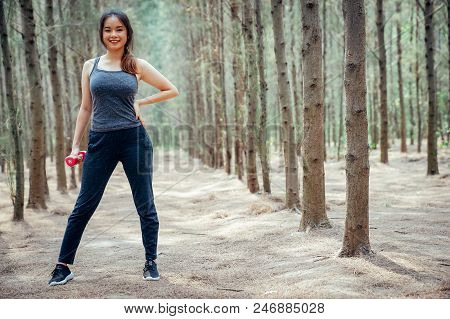 Asian Girl Is Exercising, And Playing A Drumbell At The Weekend In A Pine Forest Green And Lush Beau