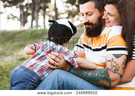 Dark-haired Hipster Family In Nature, Bearded Dad With Tattoos And Stylish Clothes.