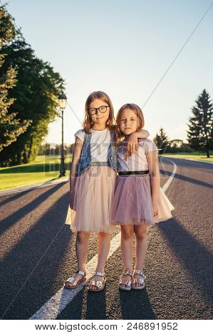 Two Attractive Girls Standing On The Road And Hugging. Sisters And Friends Love Concept.