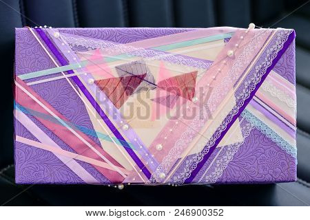 Handmade Gift Box Wrapped With Purple Paper And Decorated With White Beads On Dark Leather Sofa. Top