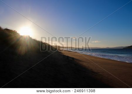 Sunny Summer White Sandy Beach With Sun Rising In Distance, Clean Calm Ocean With Waves Breaking And