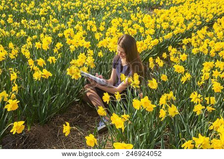Teenager Girl Paints Flowers, Sitting In Blooming Field.