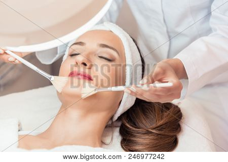 High-angle close-up view of the face of a beautiful woman during anti-aging facial massage with soft brushes in a modern cosmetic center