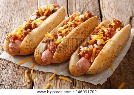 Three Tasty Chili Hot Dogs With Cheddar Cheese, Onion And Spicy Sauce Close-up On Paper. Horizontal