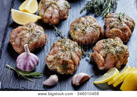 Close-up Of Raw Rabbit Ballotine Prepared To Be Cooked On A Black Slate Plate With Herbs And Spices,