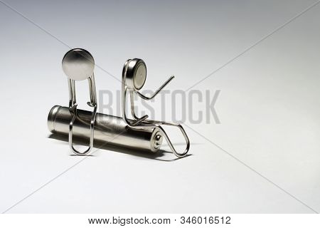 Two Paper Clips In The Form Of Men Sit On A Cylindrical Battery. Their Faces Are Made Of Round Batte