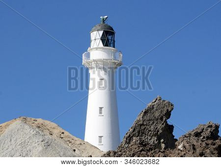 Castlepoint Lighthouse, Towering Above The Rocks Against A Clear Blue Sky.