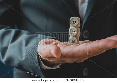 Hand Of A Businessman Holding A Stack Of Three Wooden Dices Spelling Brb.