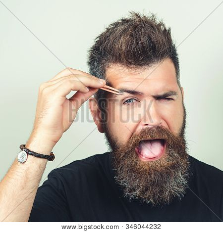 Close Up Beauty Portrait Of Bearded Concentrated Young Man Using Tweezers Isolated Over Gray Backgro