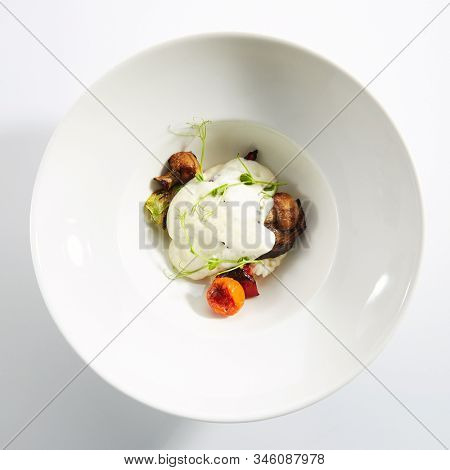 Risotto with grilled vegetables, carnaroli rice and cheese foam on white restaurant plate isolated. Traditional Italy rissoto or vegetable paella with cooked eggplants, mushrooms and greens topview