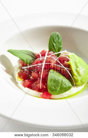 Gourmet tuna tartar with various dip and vegetables on white restaurant plate isolated. Macro shot of raw yellowfin fish tatar, luxury healthy food, seafood with cream sauce and spinach closeup