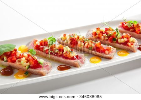 Appetizer with tuna tartar, seasonal vegetables and greens on white restaurant plate isolated. Macro photo of delicious healthy red fish tatar or tar-tar entree closeup
