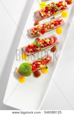 Appetizer with tuna tartar, seasonal vegetables and greens on white restaurant plate isolated. Macro photo of delicious healthy red fish tatar or tar-tar entree closeup