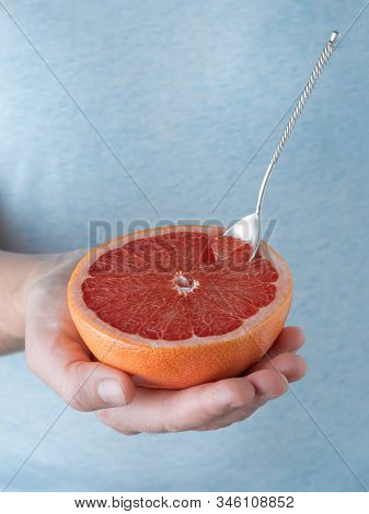 Closeup, Photo Of A Woman Holding Half Of Fresh Ripe Red Grapefruit In Her Hand. Blue Pastel Backgro