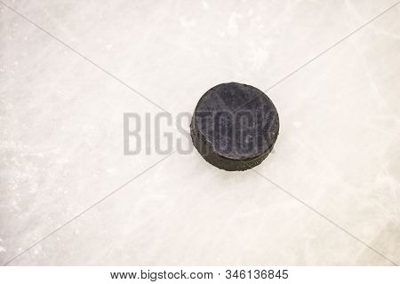 Black Ice Hocikey Rubber Puck Located On Arena Ice Rink. Ice And Puck Have Small And Deep Scratches.