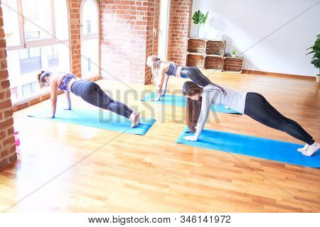 Young beautiful group of sportswomen smiling happy practicing yoga doing plank pose at gym
