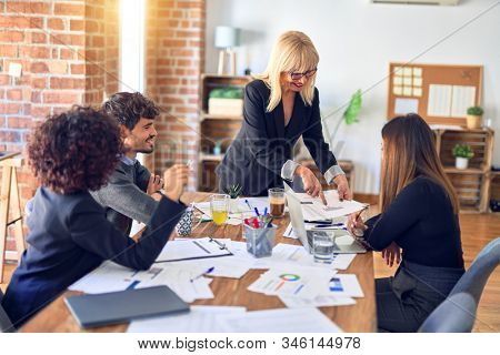 Group of business workers smiling happy and confident. Working together with smile on face. Middle age beautiful woman standing explaining documents at the office