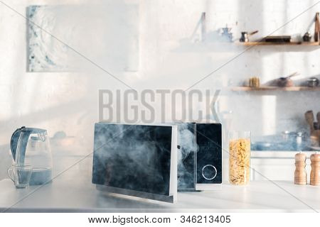Electric Kettle, Pasta, Broken And Steamy Microwave On Table In Kitchen