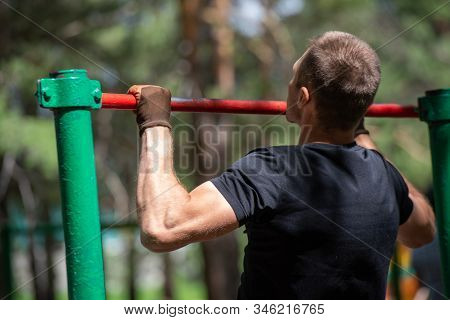 The Boy Pulls Himself Up On The Crossbar In The Park. Back View