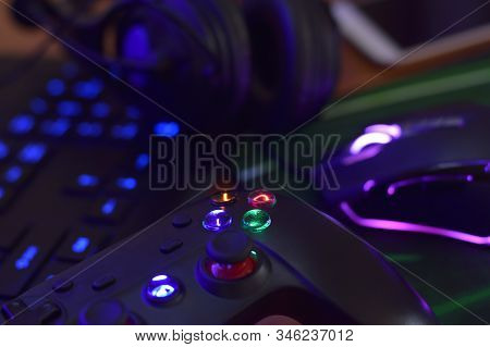 Modern Gamepad And Gaming Mouse Lies With Keyboard And Headphones On Table In Dark Playroom Scene. E