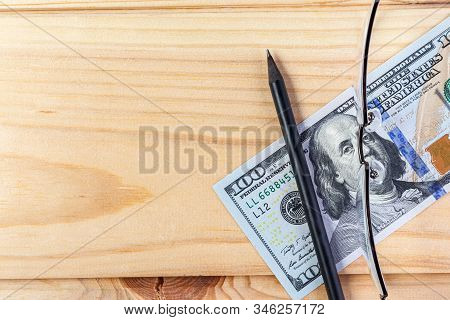 Close-up Of Glasses And A Pencil With 100 Us Dollars On A Wooden Frn. Financial Background Money Bac