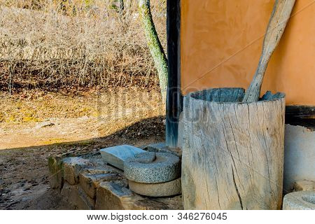 Wooden Mortar And Pestle Next To Stucco Building In Public Park.