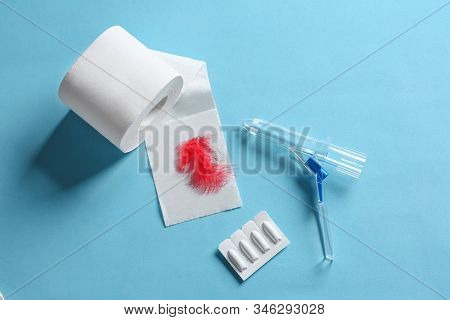 Anoscope, Suppositories And Toilet Paper With Red Feather On Light Blue Background, Flat Lay. Hemorr