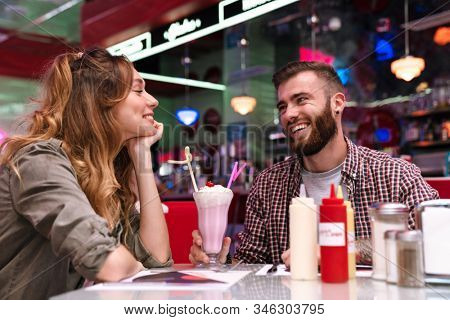 Image of a happy young loving couple sit in retro bright cafe drinking cockail indoors.