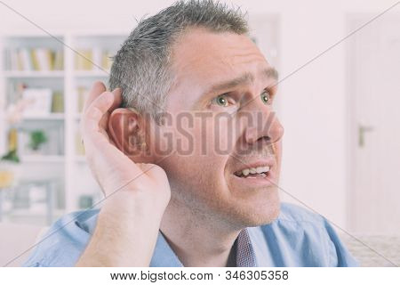 Man wearing deaf aid in ear attempting to hear something
