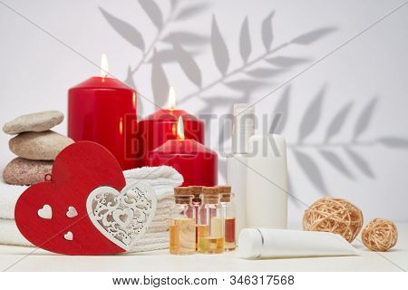Spa still life with creams, essential oils, burning red candles, hearts on light background with shadow from plant. Healthy lifestyle, body care, Spa treatment. Valentine's Day. Honeymoon. Wedding