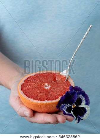 Closeup, Photo Of A Woman Holding Half Of Fresh Ripe Red Grapefruit In Her Hand. Blue Pastel Backgro