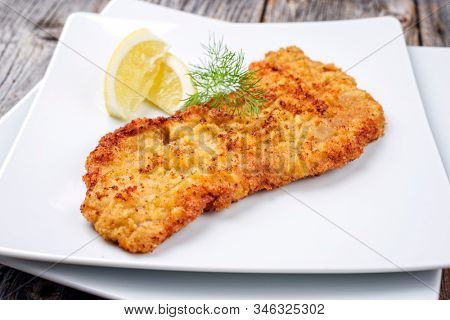 Traditional deep fried Wiener schnitzel from veal topside with lemon slice and herb offered as closeup modern design plate 