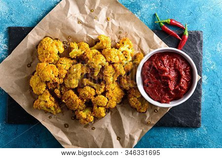 Top View Of Vegetarian Cauliflower With Chili Sauce And Pepper On Craft Paper On Blue Background