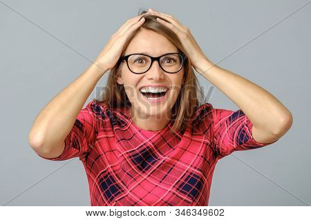 Portrait Of Stunned Woman In Red Dress, Holding Hands On Head, Being Surprised And Amazed