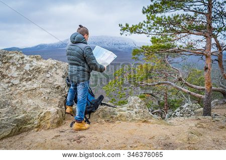 Well-dressed Man Working With Laptop Sitting On The Rocky Mountain On Beautiful Scenic Clif Backgrou