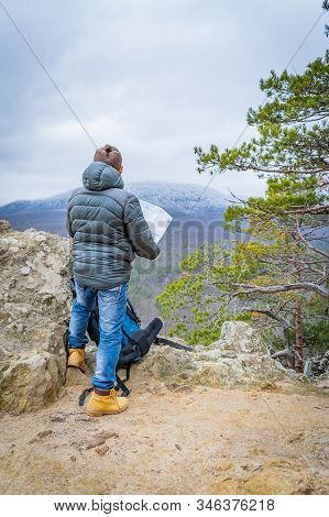 Well-dressed Man Working With Laptop Sitting On The Rocky Mountain On Beautiful Scenic Clif Backgrou