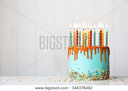Colorful birthday cake with lots of candles and orange drip icing