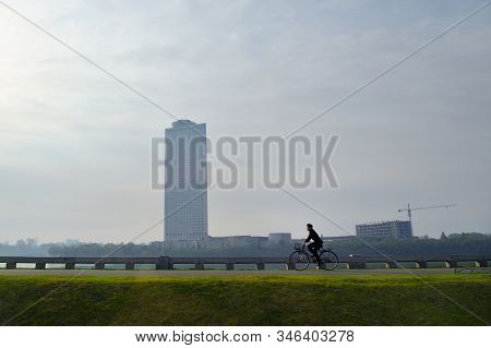 Pyongyang, North Korea - May 1, 2019: Local Man Riding On A Bike Along Taedong River At Sunrise. Mod