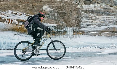 Man Is Riding Bicycle Near Ice Grotto. Rock With Ice Caves Icicl