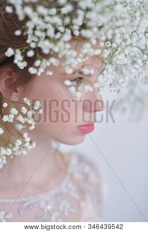 Beautiful tender girl with lovely freckles on her face and in a gypsophila wreath on a white background. Inspiration of spring and summer. Perfume, cosmetics concept. Prifile portrait. 