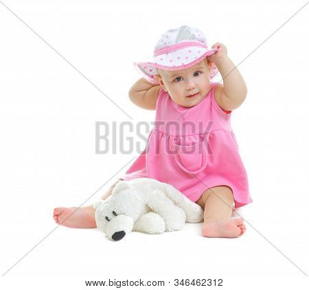 A Little Baby Girl In Pink Dress And Panama Hat Sits On White Background In Studio With Little Bear 
