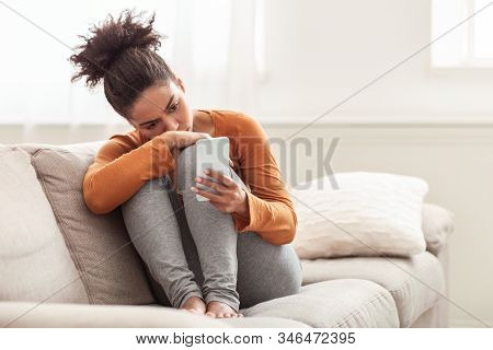 Waiting For Call. Depressed Afro Lady Holding Mobile Phone Feeling Lonely Sitting On Sofa Indoor. Se