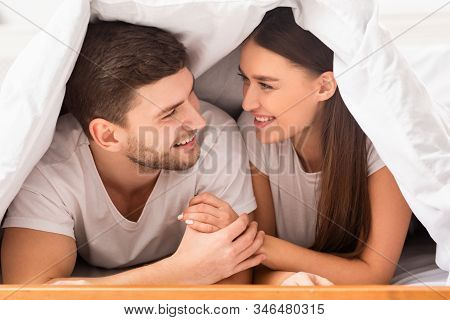 Couple Relatioship. Happy Boyfriend And Girlfriend Lying On Bed Covered With Blanket In Bedroom. Sel