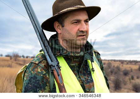Hunter Man In Camouflage With A Gun During The Hunt In Search Of Wild Birds Or Game. Autumn Hunting 
