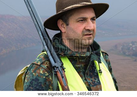 Hunter Man In Camouflage With A Gun During The Hunt In Search Of Wild Birds Or Game. Autumn Hunting 